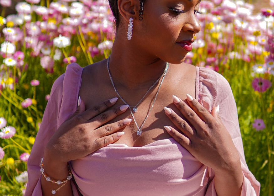 Woman in a pink dress standing in a field of flowers, wearing a necklace with a heart pendant.